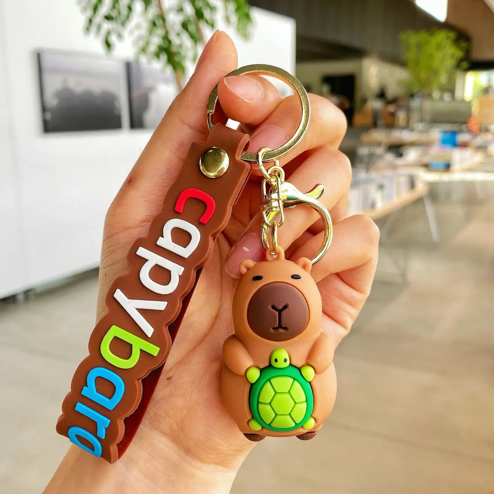 Hand holding a kawaii keychain with a bear and turtle design, branded 'Capybara'.