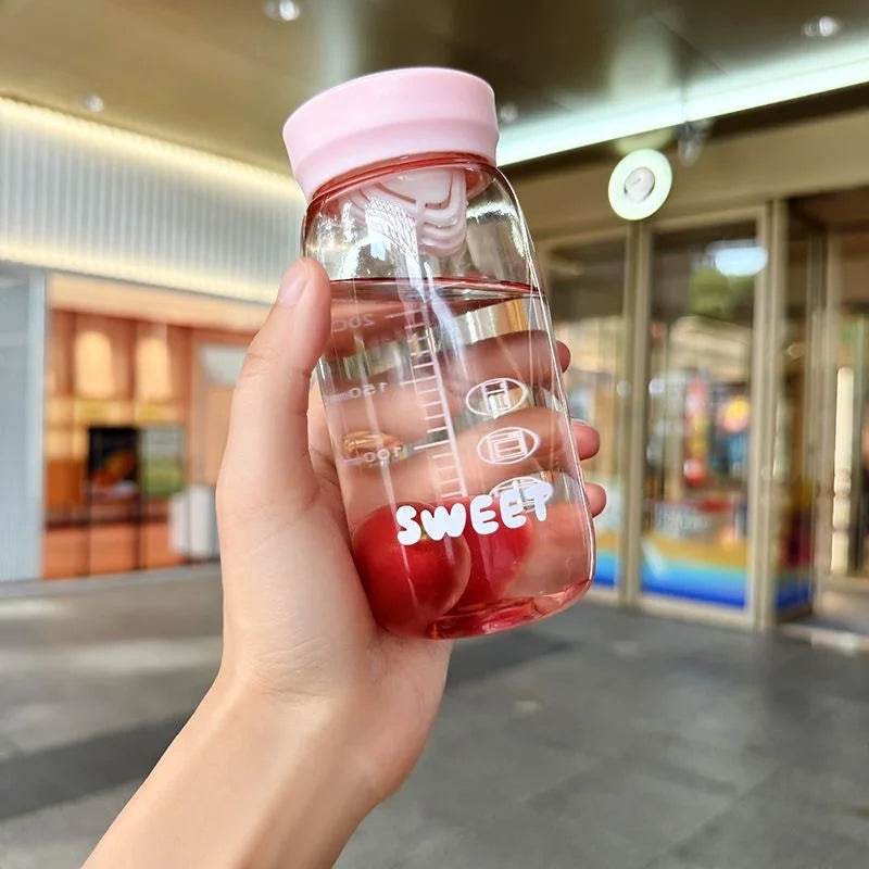 Clear Kawaii water bottle with pink cap and 'SWEET' text held in a hand, blurred indoor background