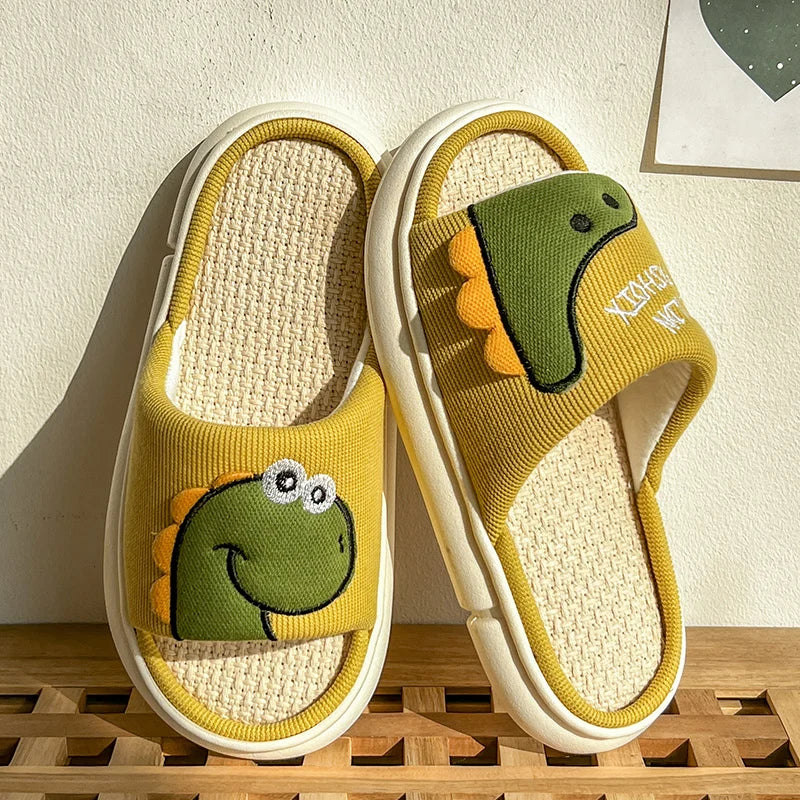 Pair of yellow slippers with green kawaii dinosaur designs on a wooden surface.