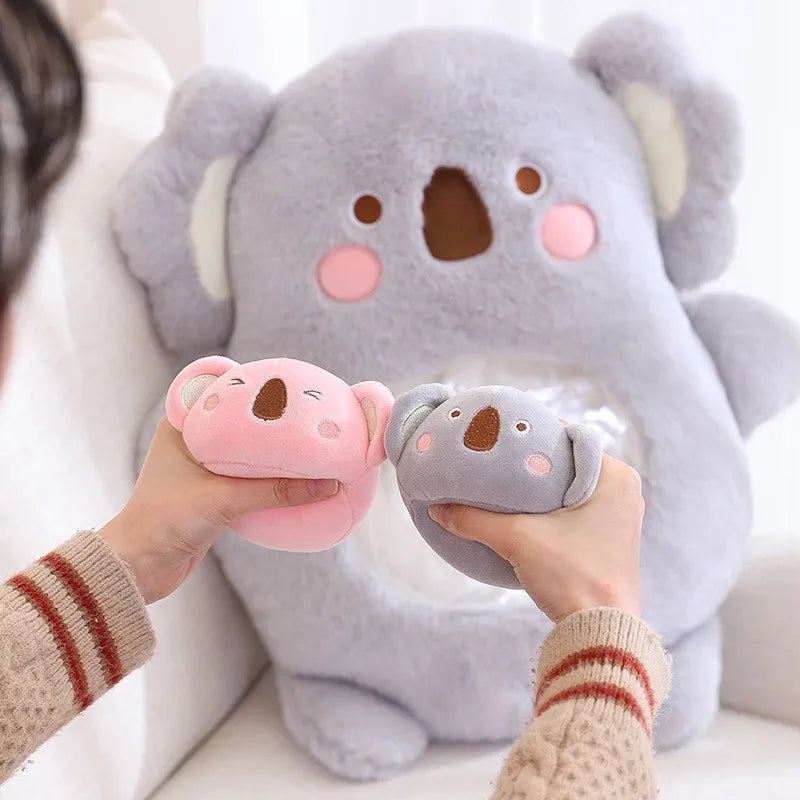 Two small koala plush toys held by hands with a large koala kawaii plush toy in the background.