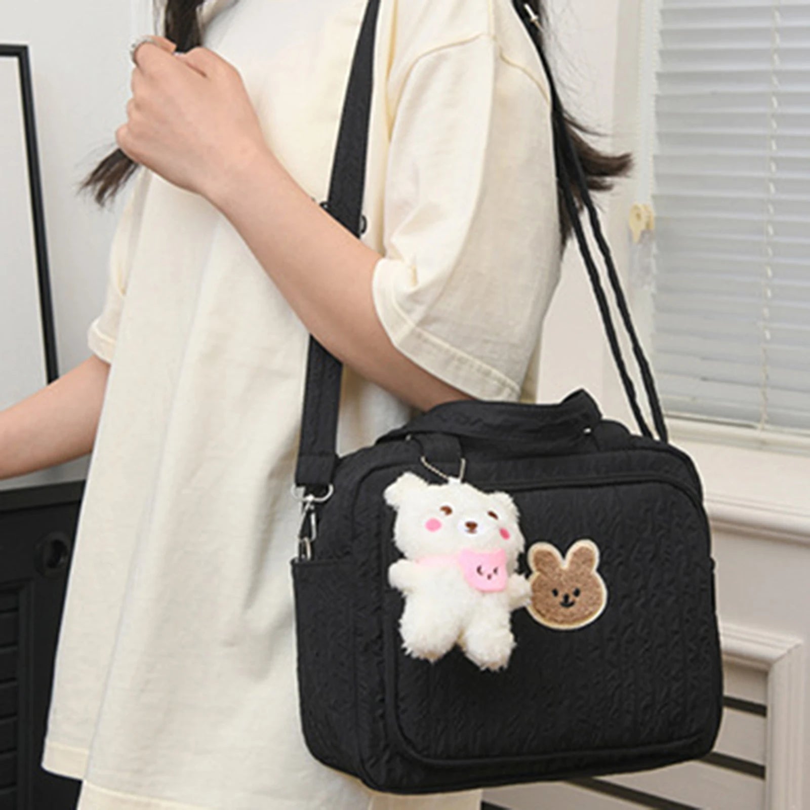Black quilted handbag with Kawaii plush toy bear and rabbit attachments held by a person.