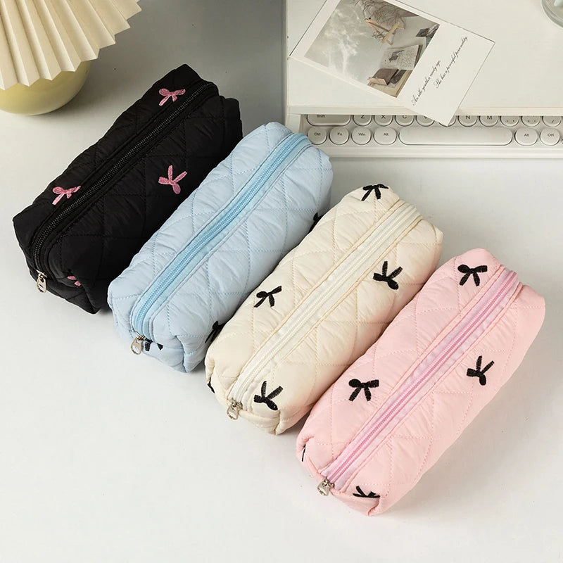 Five quilted pencil cases in black, blue, beige, and pink with kawaii bow designs on a light surface.