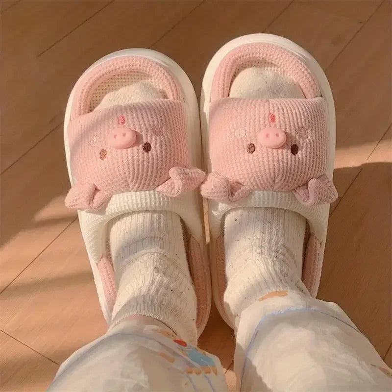 Pink piggy-themed kawaii slippers worn with white socks on a wooden floor.