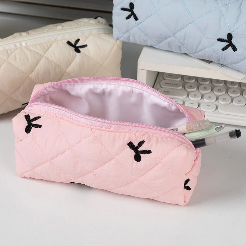 Pink quilted kawaii pencil case with black embroidered designs on a white surface.
