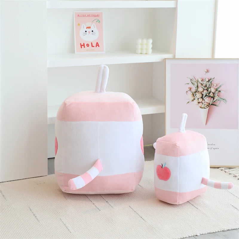 Two pink and white kawaii plush toys resembling milkshakes on a wooden floor.