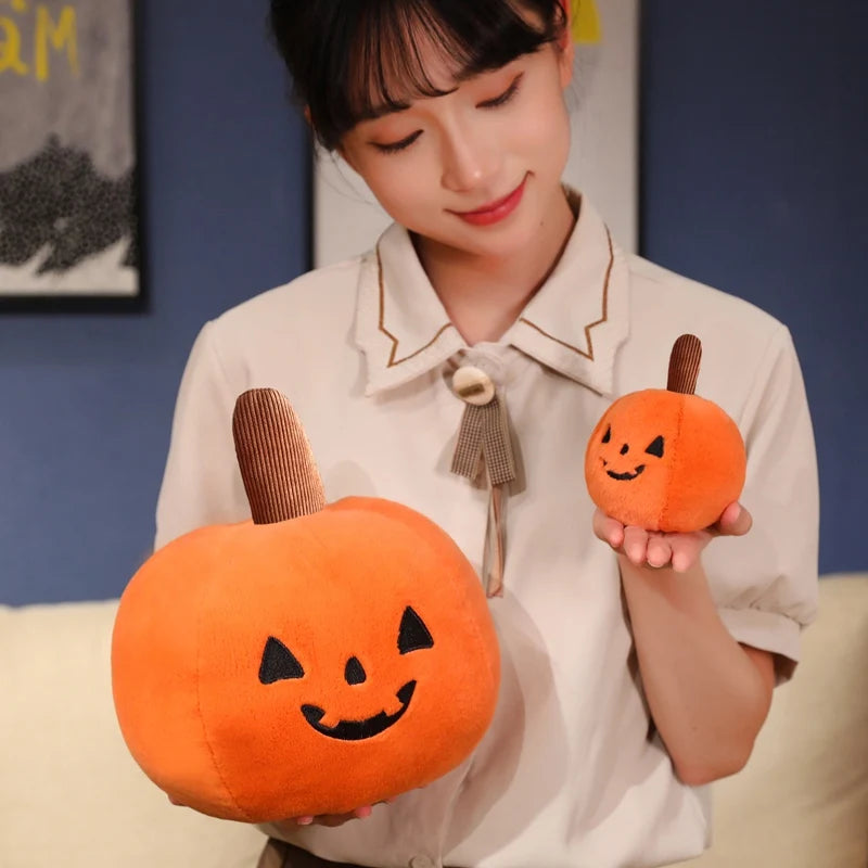Person holding two kawaii plush pumpkins with smiling faces against a blue wall.