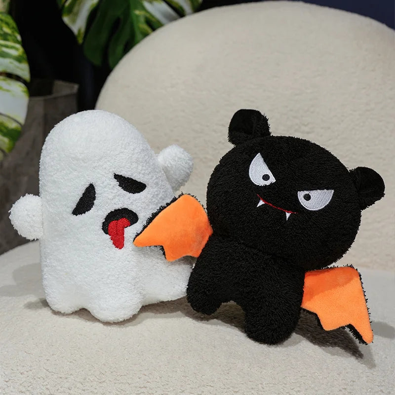 White ghost and black cat plush kawaii toys with orange bat wings on a light surface.