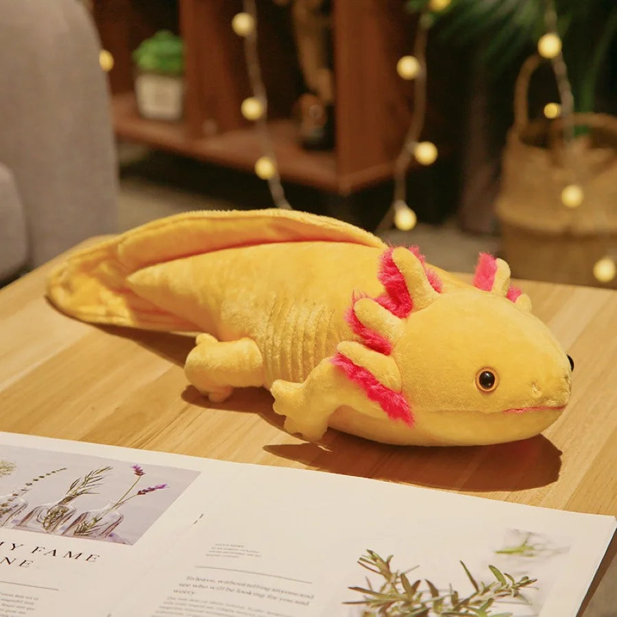 Yellow plush axolotl kawaii toy on a wooden surface with a magazine underneath
