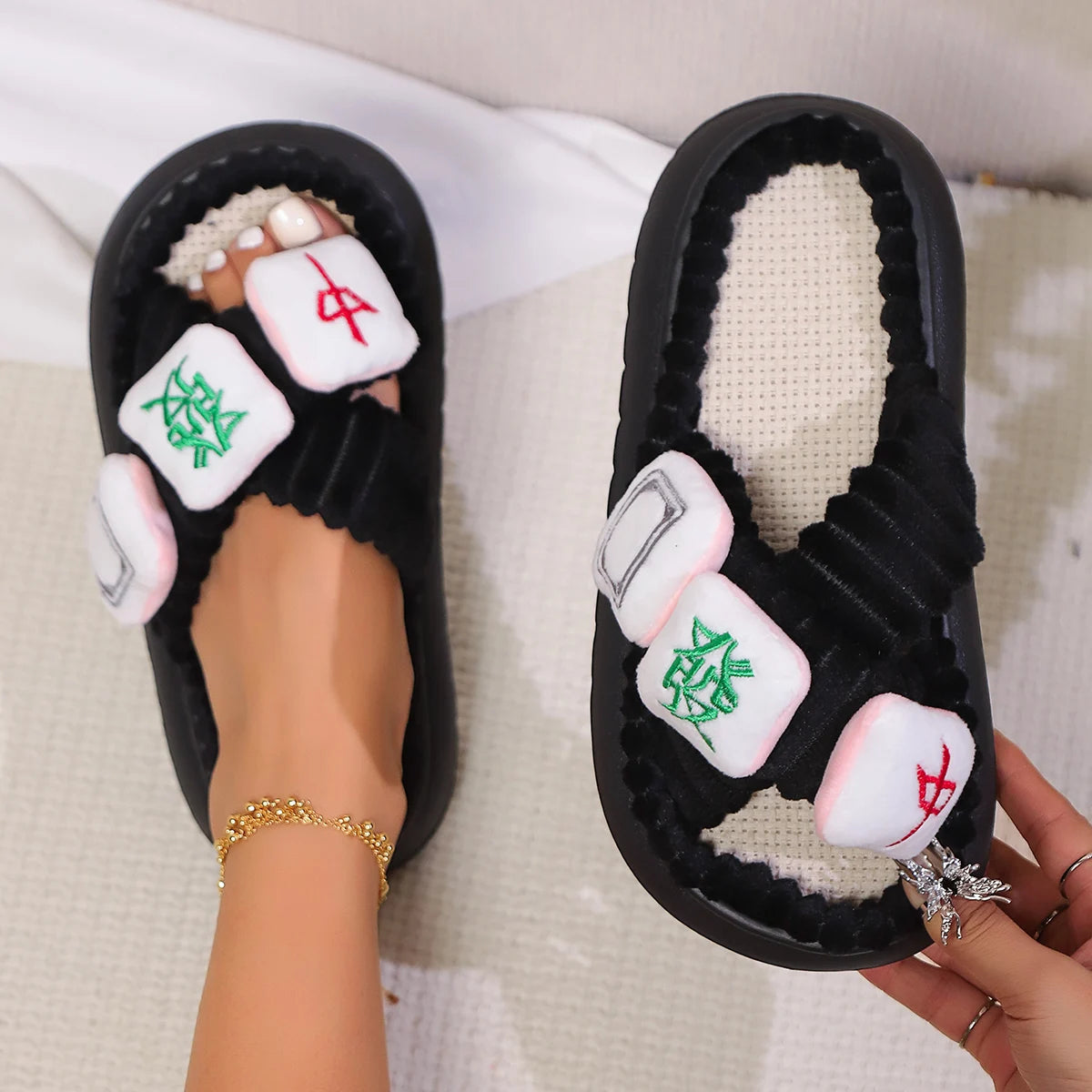 Black slippers with dice kawaii designs worn by a person on a light-colored surface.