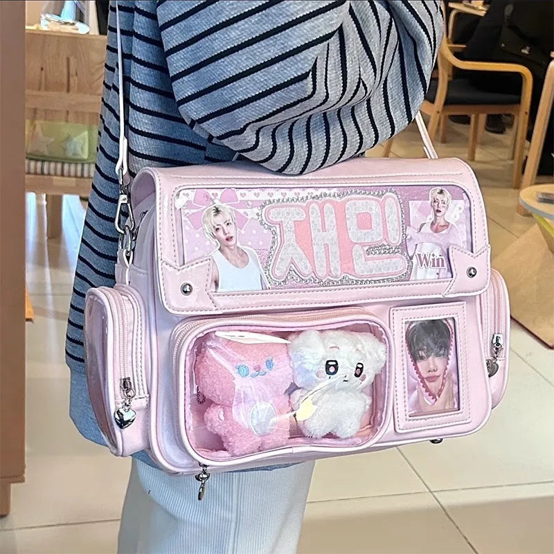 Pink backpack with images of people and a Kawaii plush toy, held by a person in a striped sweater.