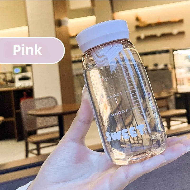 Clear Kawaii water bottle with white cap held in a hand, blurred indoor background