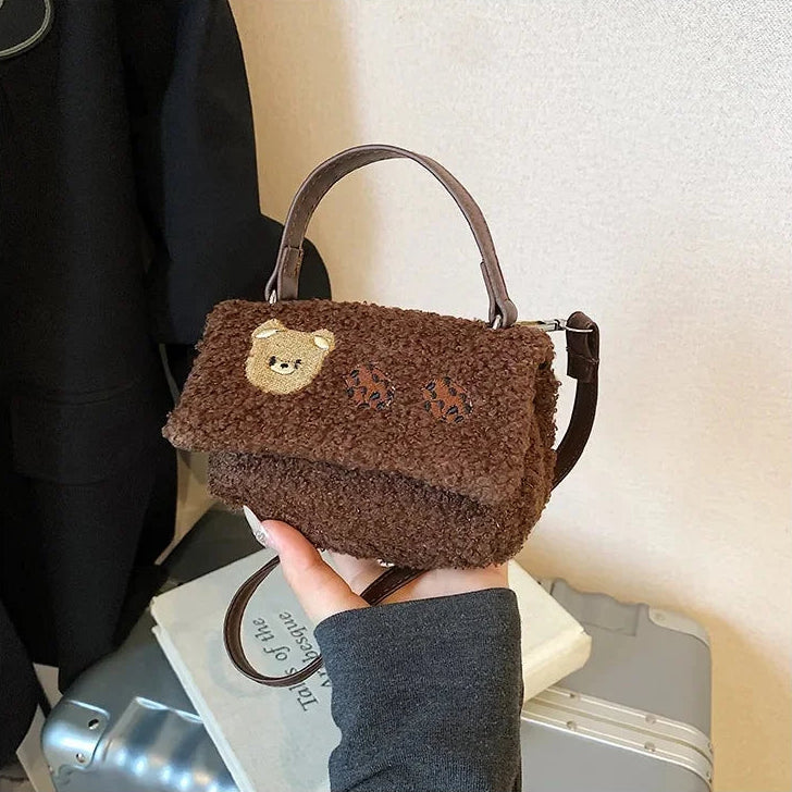 Brown Kawaii teddy bear-themed handbag held by a person against a neutral background