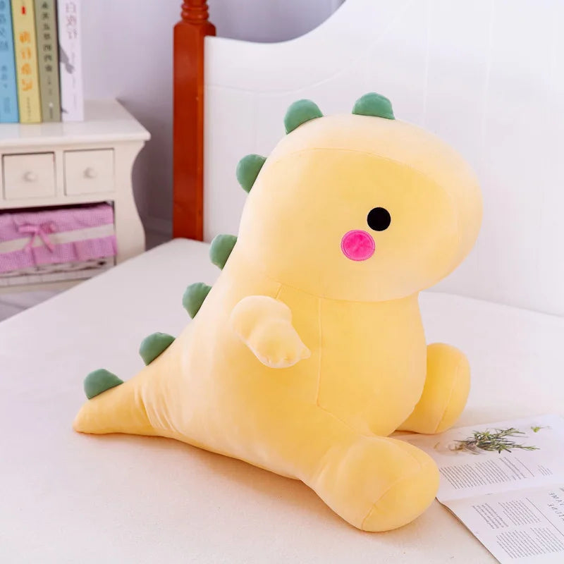 Yellow dinosaur kawaii plush toy on a bed with books and a nightstand in the background