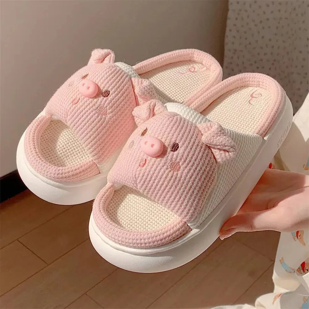 Pink children's kawaii slippers with pig design held by a hand on a wooden floor.