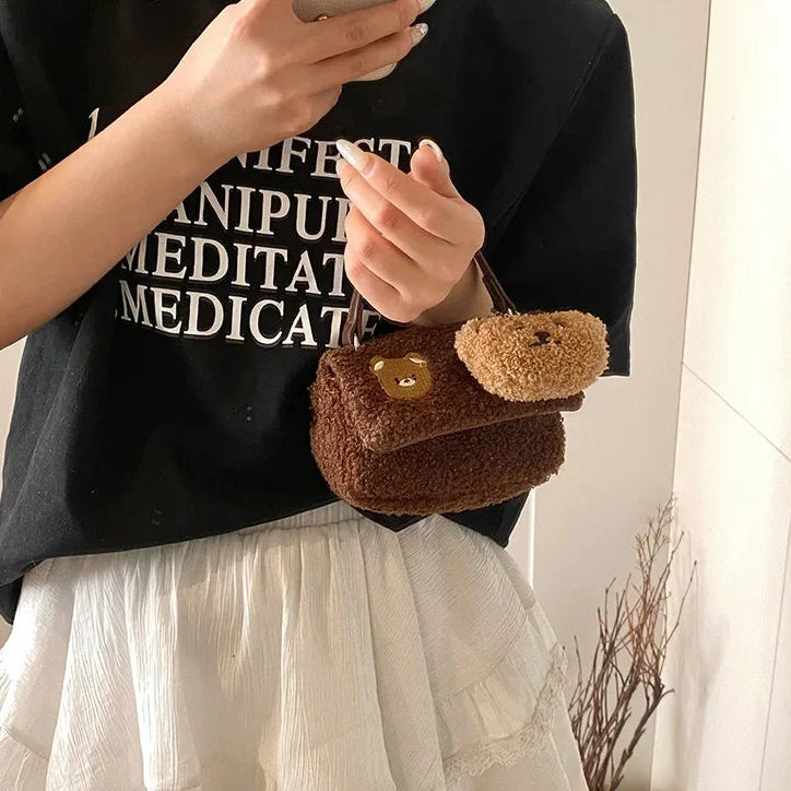 Person holding a small brown bag with a Kawaii teddy bear design against a neutral background