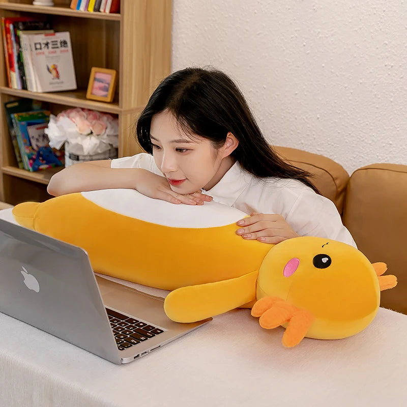 Woman sitting on a couch with a large yellow kawaii plush toy resembling a duck next to a laptop.