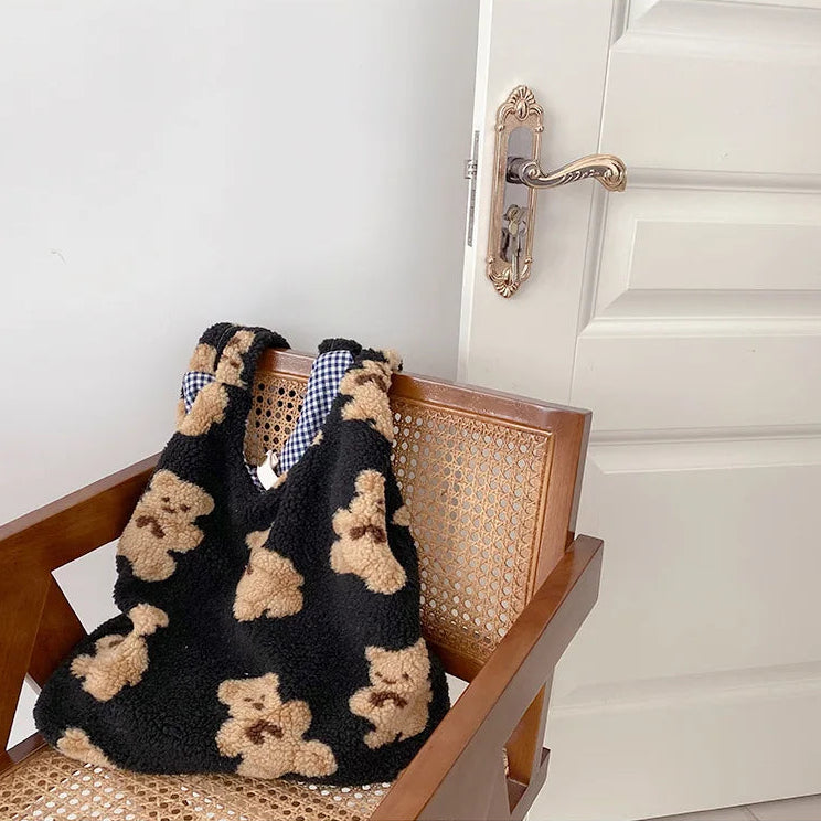 Black slippers with kawaii teddy bear pattern on a wooden chair next to a white door.