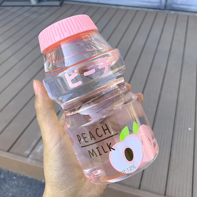 Hand holding a transparent Kawaii-inspired bottle with pink cap labeled 'Peach Milk' on a wooden surface.