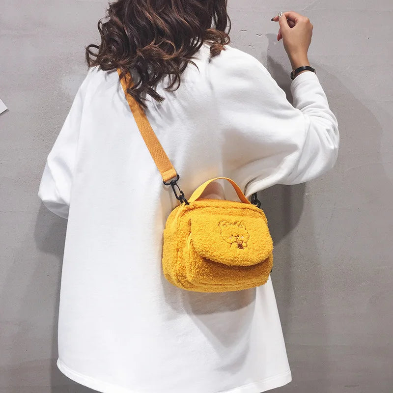 Person wearing a white sweater with a yellow fluffy Kawaii bag over one shoulder against a gray background