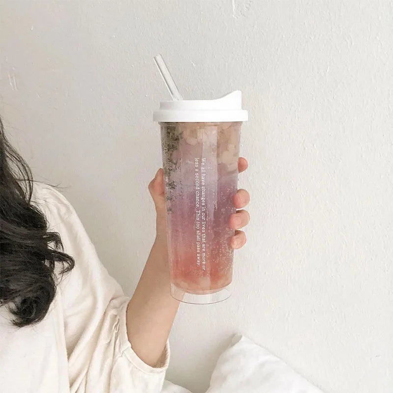 Person holding a pink iced drink in a clear Kawaii-style cup with a white lid against a plain background