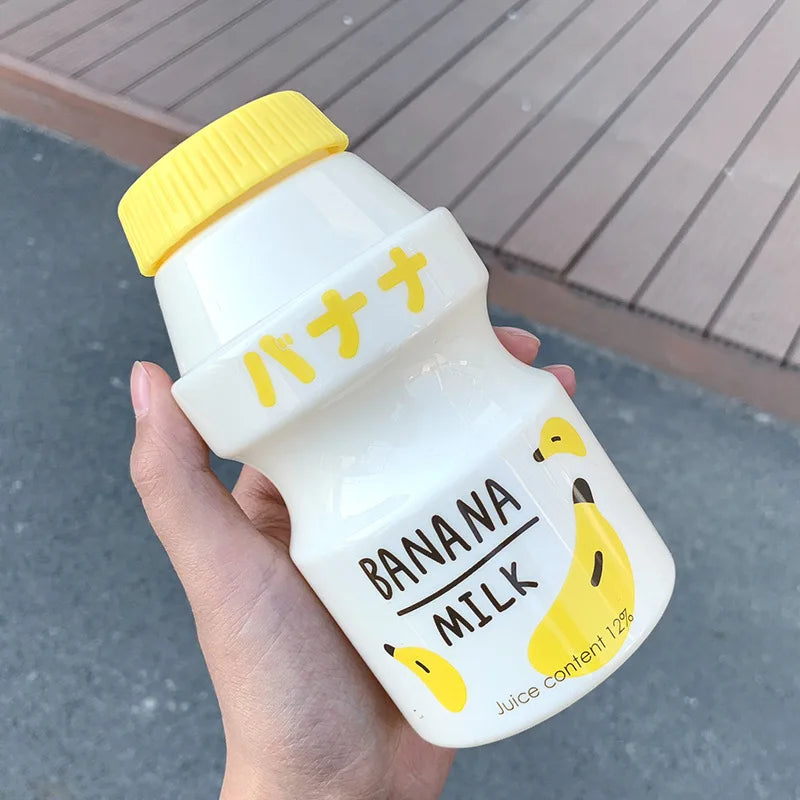 Hand holding a bottle of banana milk with a yellow cap and banana Kawaii illustrations.