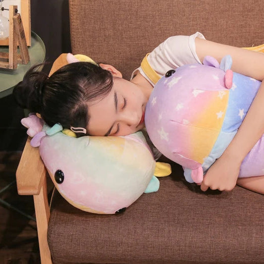 Child sleeping on a large, colorful kawaii plush toy resembling a rainbow-colored creature on a brown couch.