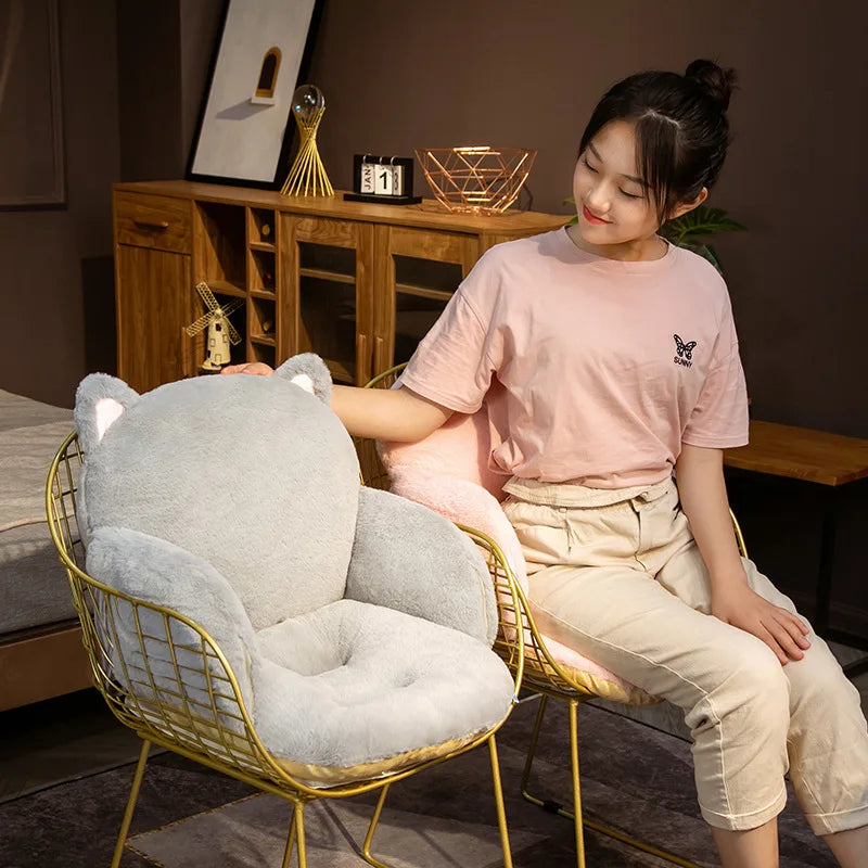 Woman sitting on a chair with a large gray cat-shaped kawaii cushion in a room.