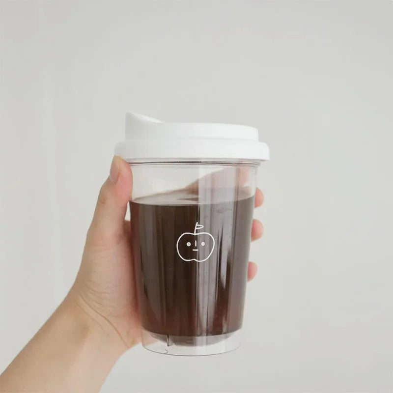 Hand holding a clear Kawaii coffee cup with a white lid against a light gray background