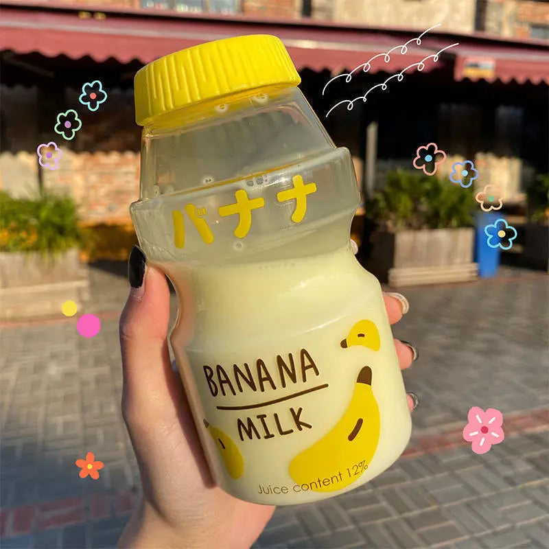 Hand holding a Kawaii bottle of banana milk with decorative elements on a blurred outdoor background