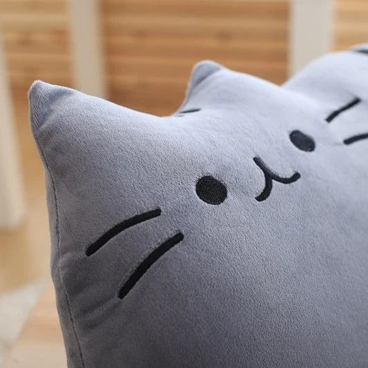 Gray cat-shaped kawaii pillow with a smiley face on a wooden floor.