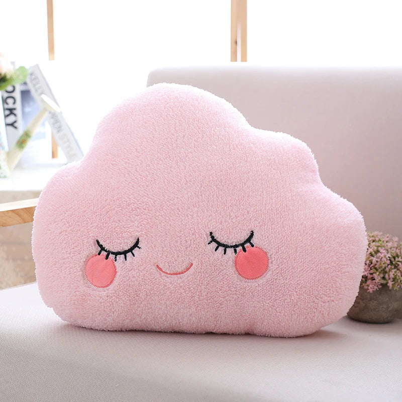 Pink cloud-shaped kawaii pillow with a smiling face on a light-colored surface.