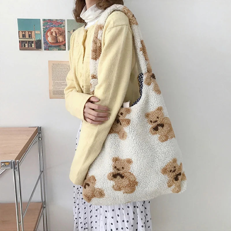Person holding a white tote bag with brown kawaii teddy bear patterns in a room.