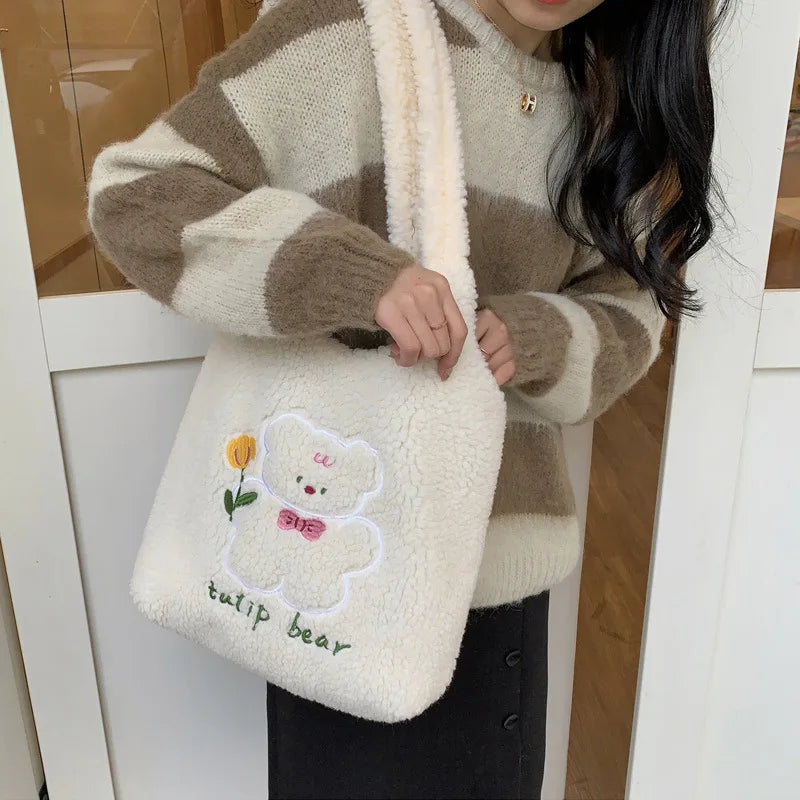 Person holding a fluffy white bag with a kawaii teddy bear design and text, wearing a brown and beige striped sweater.