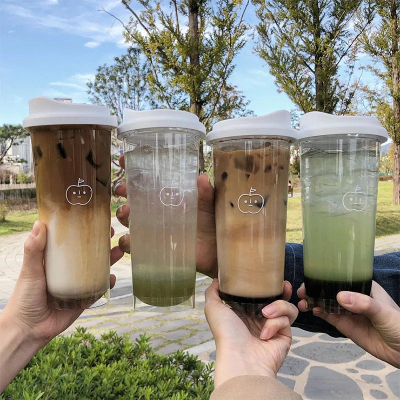 Four hands holding transparent Kawaii cups with different beverages outdoors.
