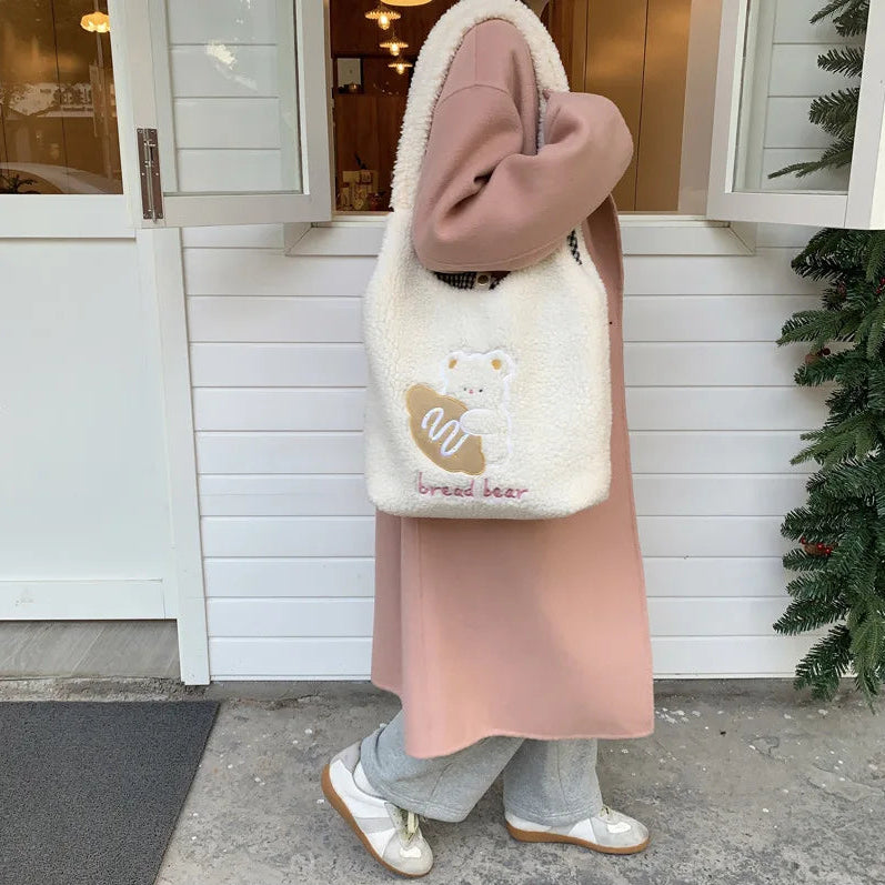 Person wearing a pink coat and holding a white fluffy bag with a kawaii bear design in front of a white building.