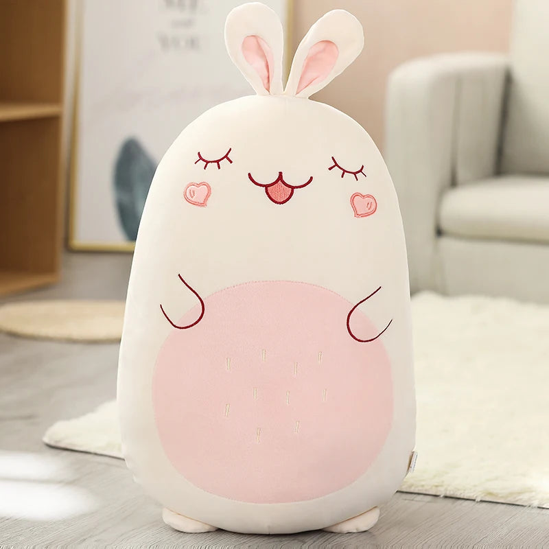 Cute plush kawaii toy with rabbit ears and a pink belly on a wooden floor.