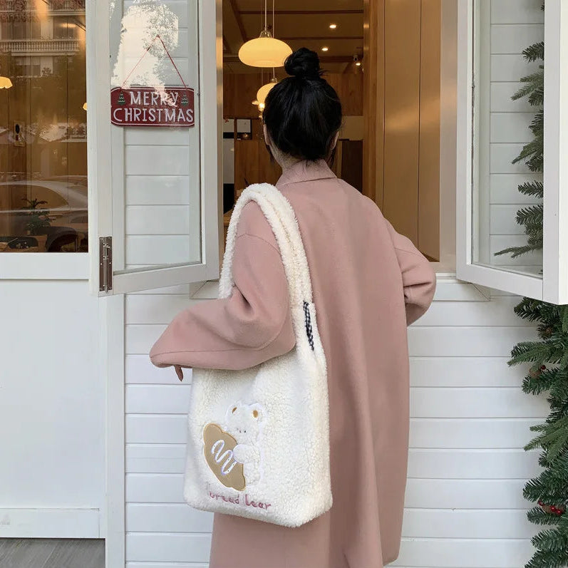 Person wearing a pink coat holding a white tote bag with a kawaii bear design, standing in front of a Christmas-themed door.