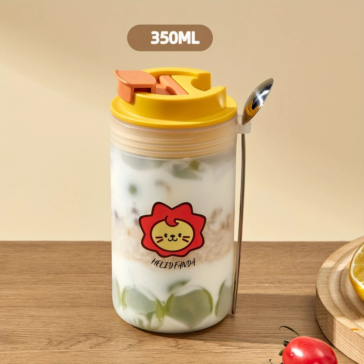 Transparent tumbler with a yellow lid and straw, featuring a Kawaii cartoon lion design, on a wooden surface.