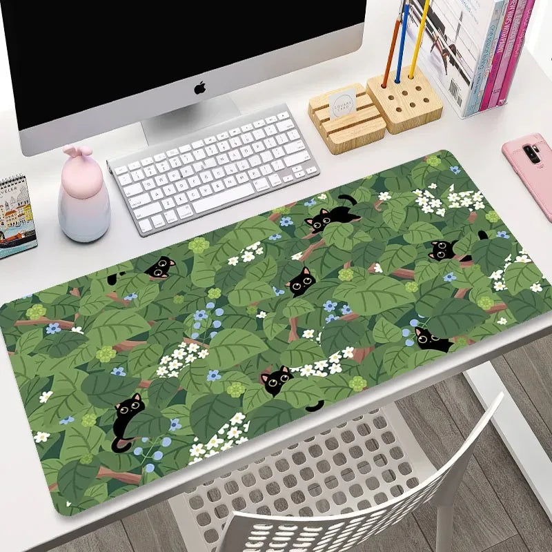 Desk setup with a green desk mat featuring Kawaii black cat illustrations, keyboard, and computer monitor.