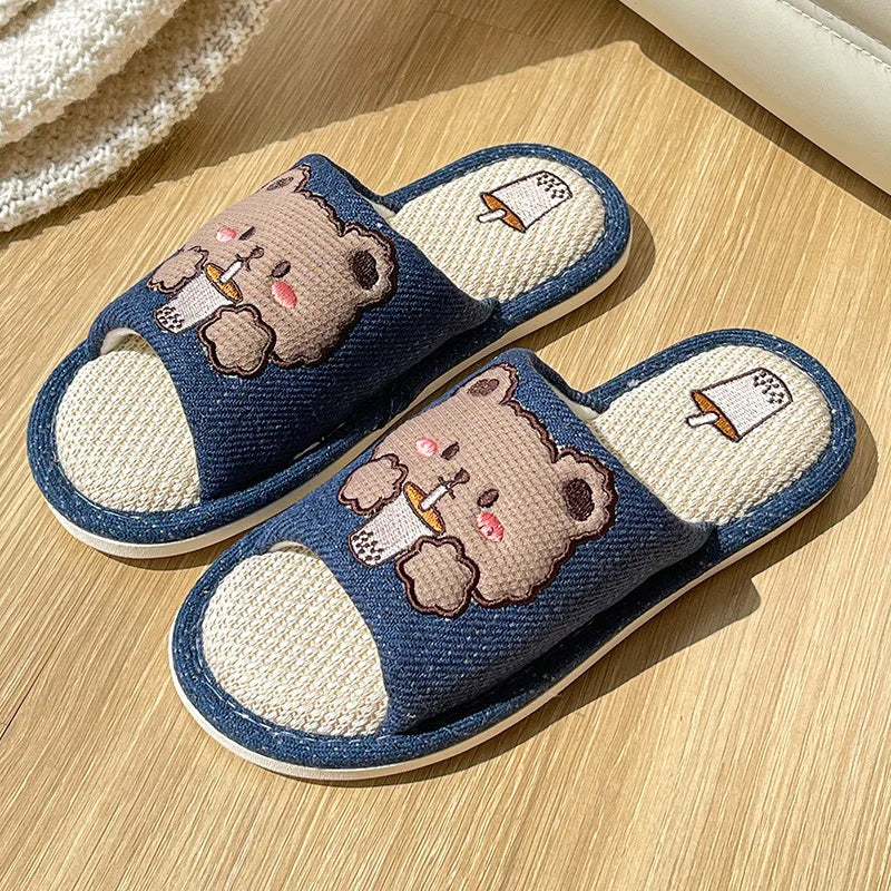 Pair of blue slippers with kawaii bear illustrations on a wooden floor.