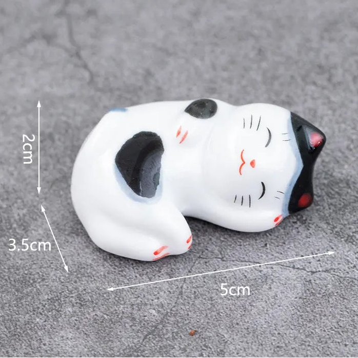 Small white kawaii cat figurine with black spots on a gray surface, showing measurements.