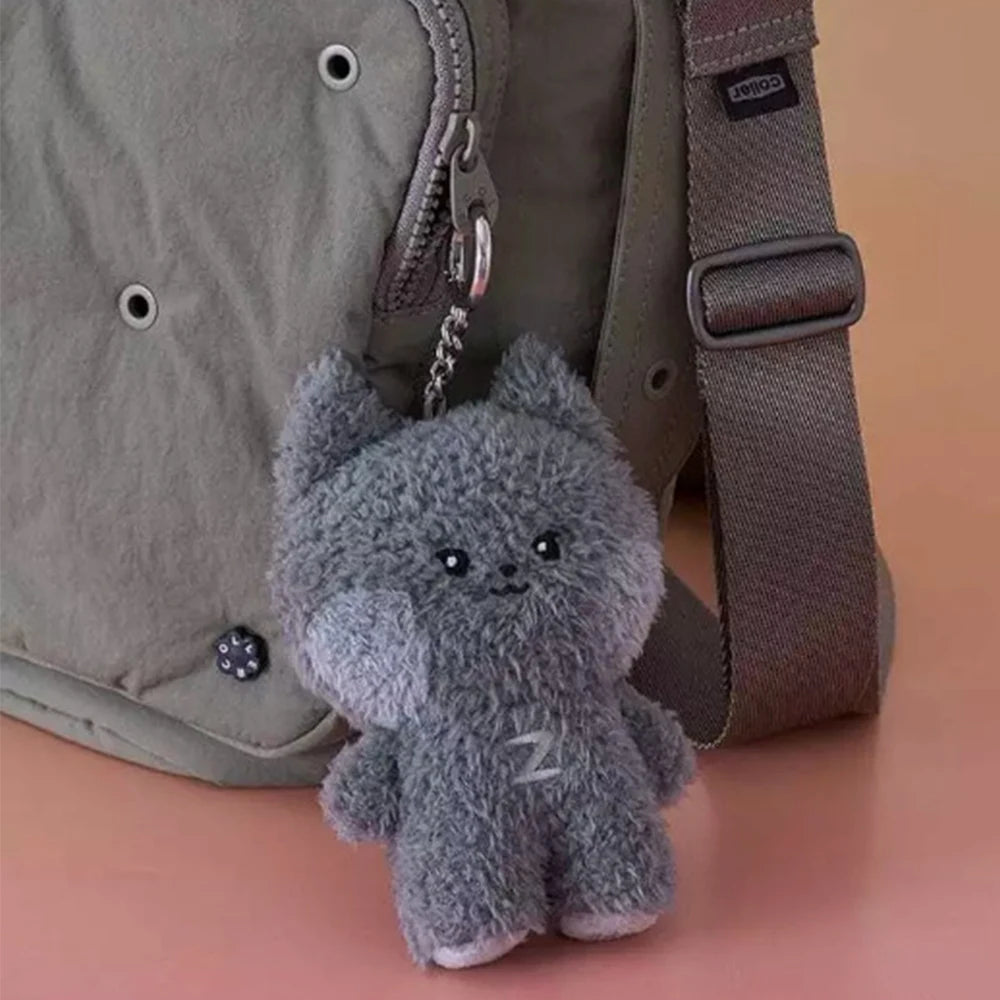 Gray kawaii plush cat keychain attached to a gray bag on a pink surface