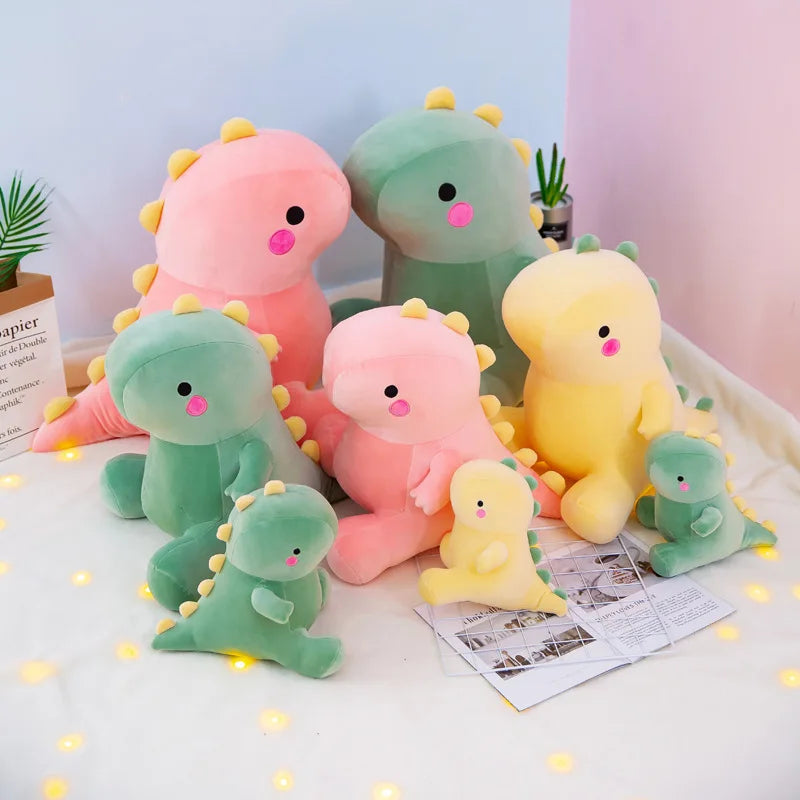 Set of colorful dinosaur kawaii plush toys on a light surface with a soft pink background.