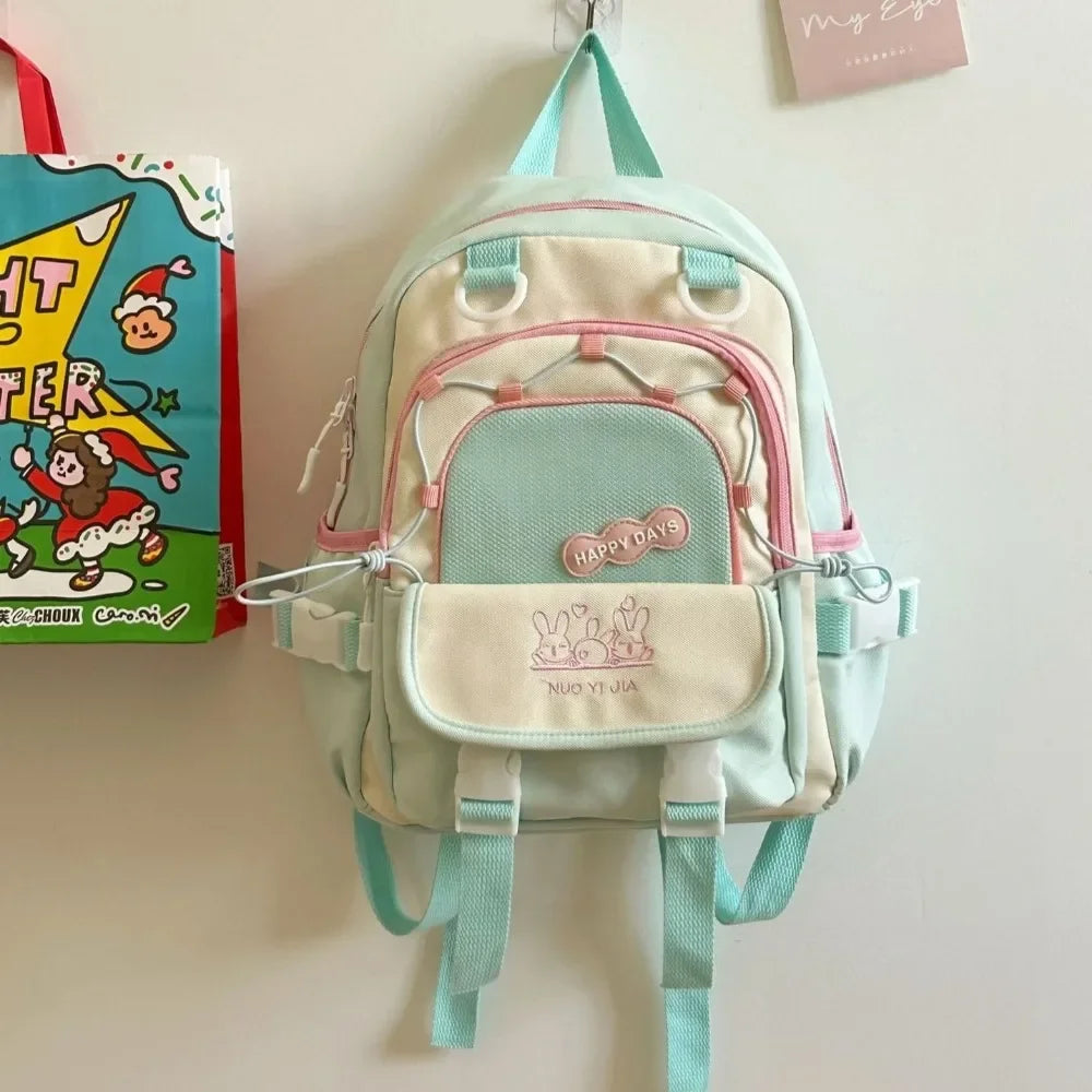 Small Kawaii backpack with pink and green accents hanging on a hook against a light background.