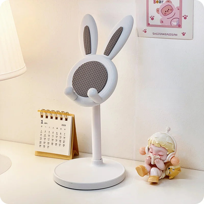 White rabbit-shaped kawaii phone stand on a desk with a calendar and small figurine in the background.
