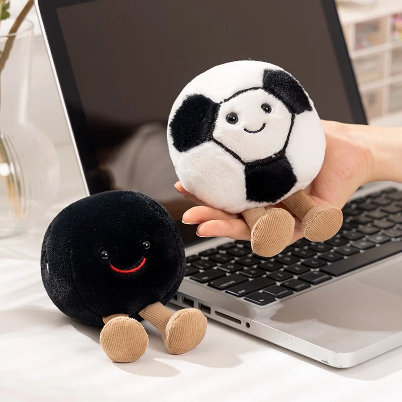Two plush kawaii toys, one black and one white with black spots, held in front of a laptop.
