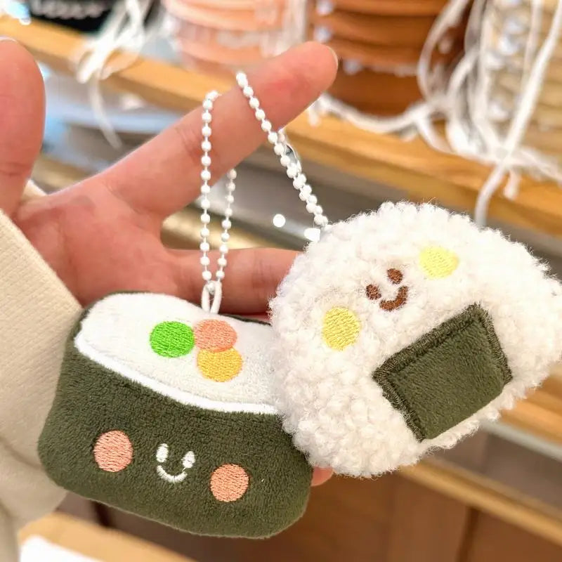 Two kawaii plush rice ball keychains with a hand holding them, blurred indoor background
