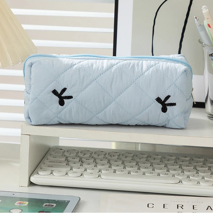 Light blue quilted kawaii pouch with black rabbit ears on a desk with a keyboard and tablet.