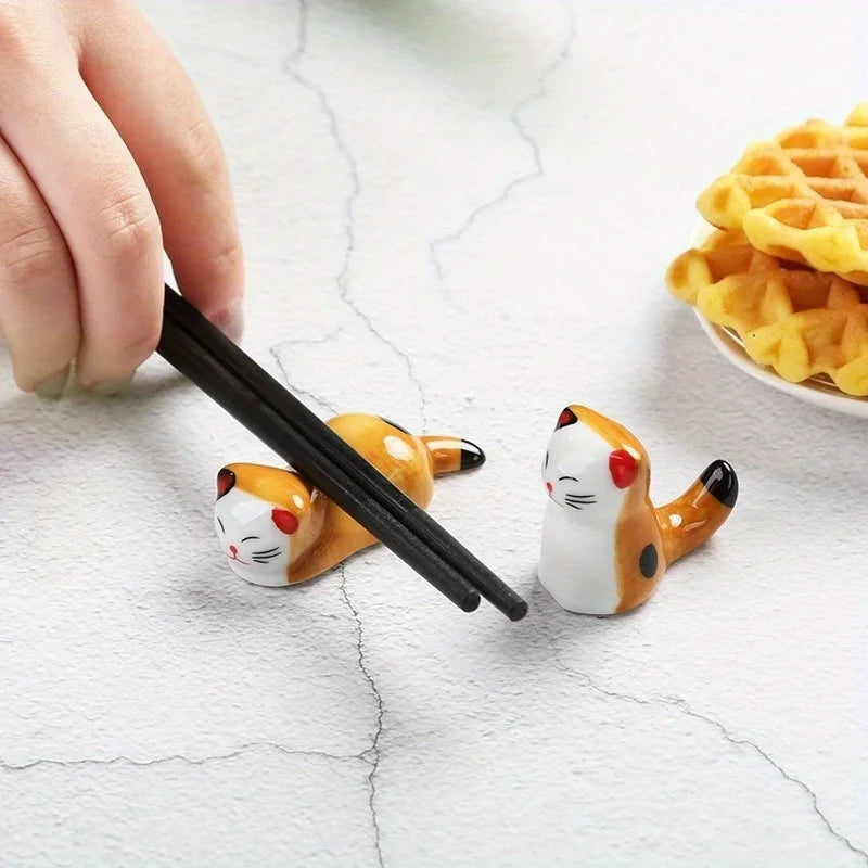 Kawaii cat-shaped chopstick rest with a hand using black chopsticks on a light surface.