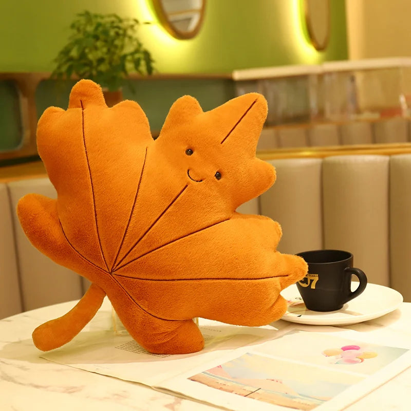Orange leaf-shaped kawaii plush toy on a table with a cup and saucer in a cozy room.